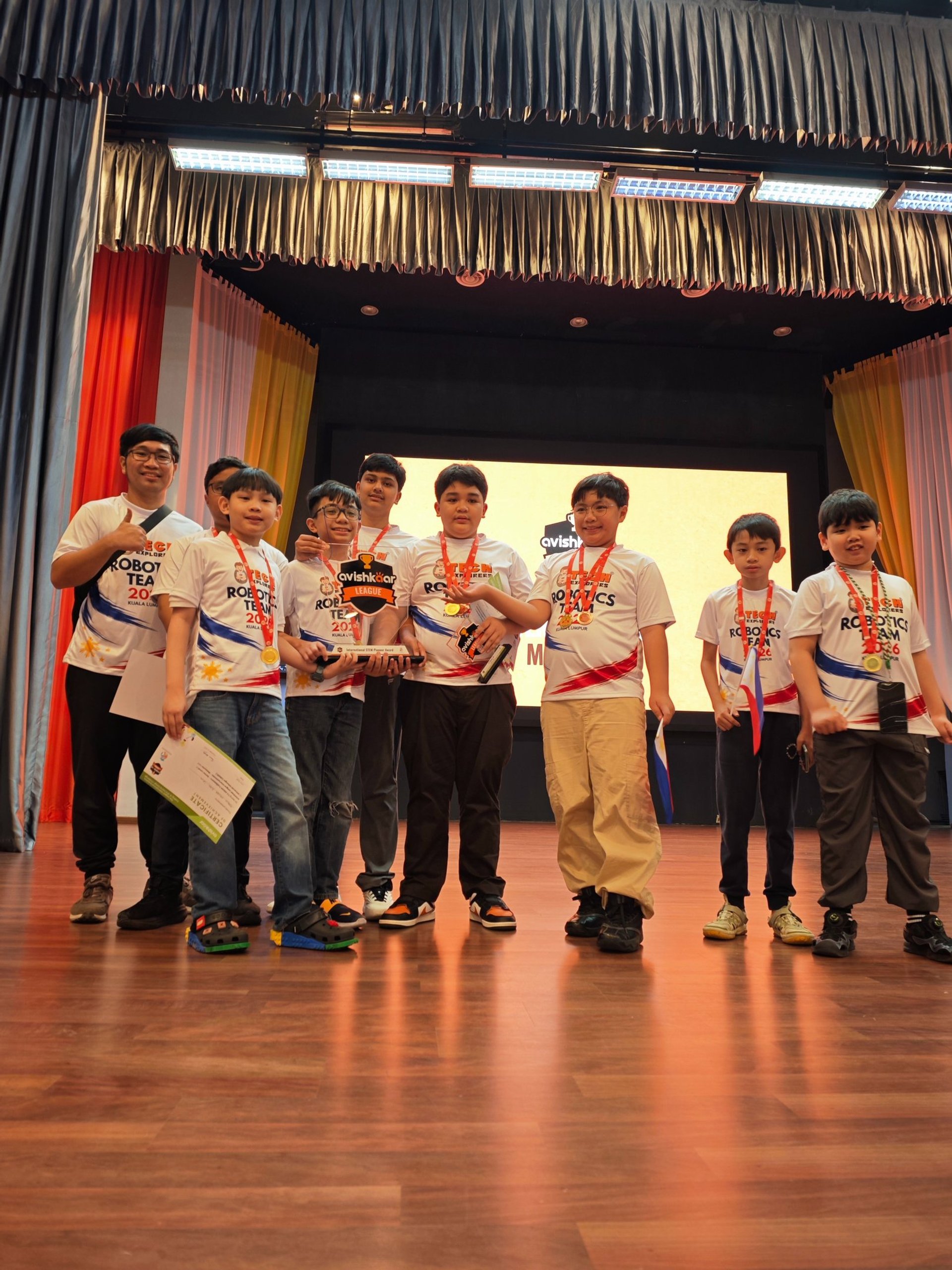 Tech Explorers robotics team celebrating on stage with trophy and medals